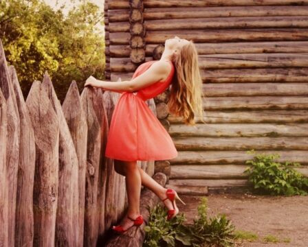 woman-in-orange-dress-leaning-against-wooden-fence